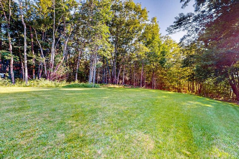 The farmhouse's broad green lawn sloping toward the wooded shoreline of the cove in Penobscot, Maine.