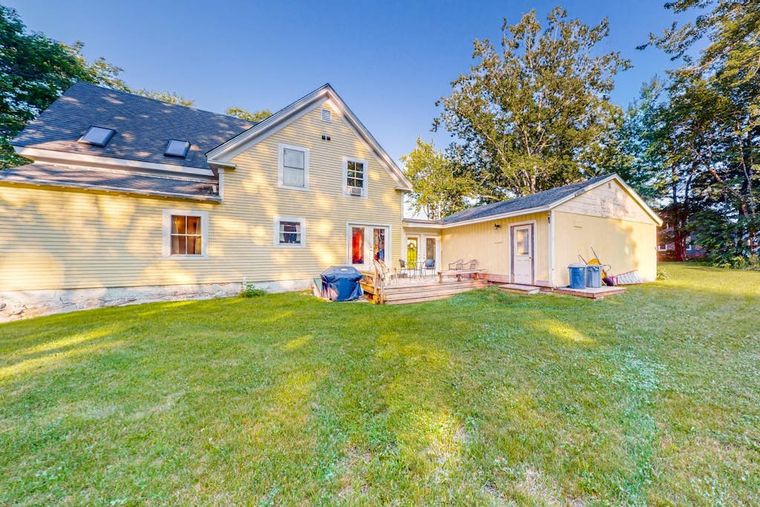 Back of the farmhouse with a wooden deck, gas grill, lawn, and detached barn-garage.