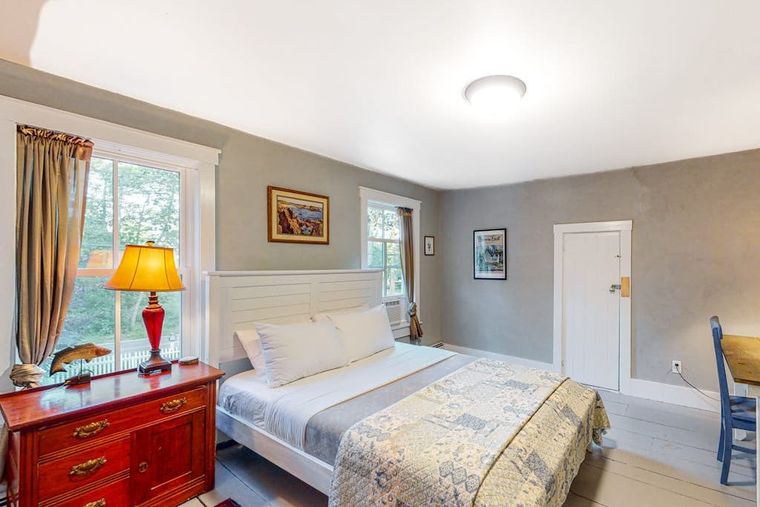 Sage-walled bedroom with a king bed, antique dresser, and white plank floors.