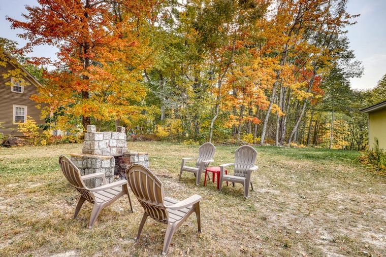 Stone firepit and Adirondack chairs on the lawn beneath bright autumn maples.