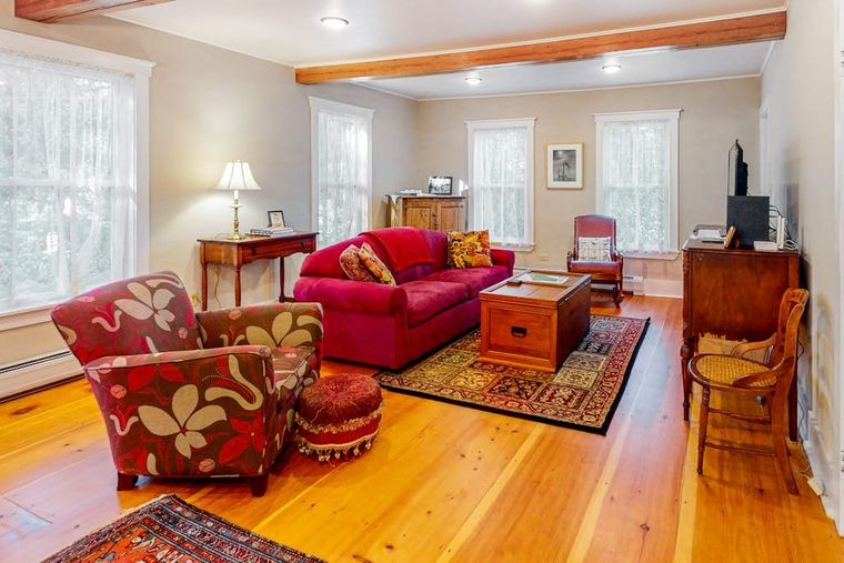 Living room with exposed beams, honey pine floors, and a red sofa on an antique rug.