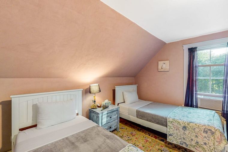 Cozy twin bedroom with sloped terracotta-toned ceilings and two white beds.